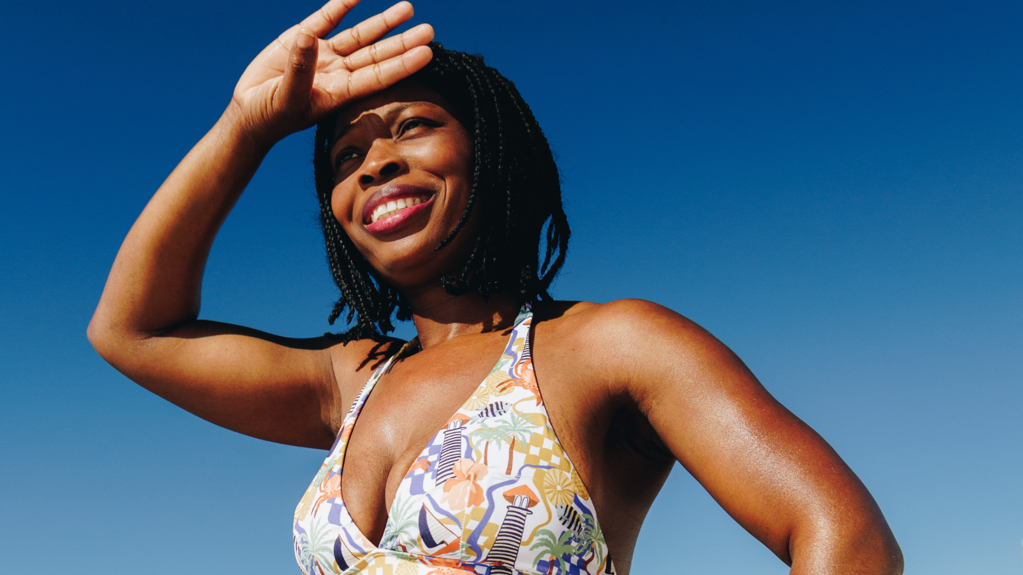 Woman in a colorful bikini standing on a beach with clear blue sky and ocean.